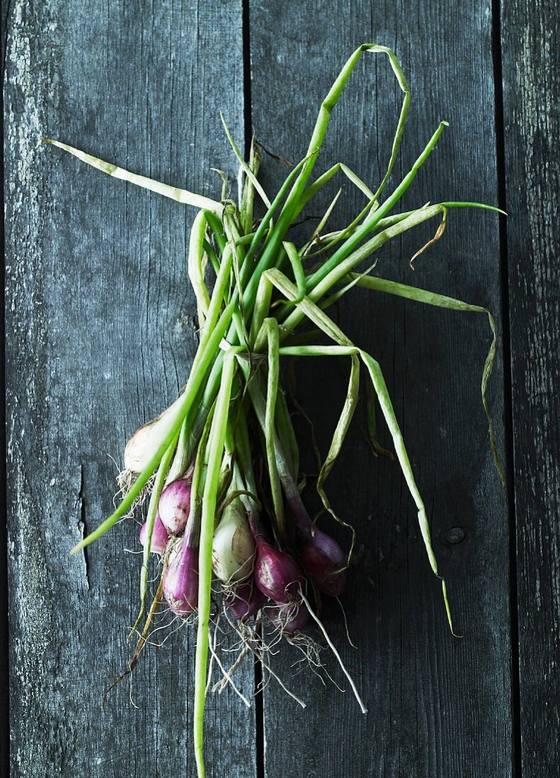 A bunch of spring onions on a wooden surface (seen from above)