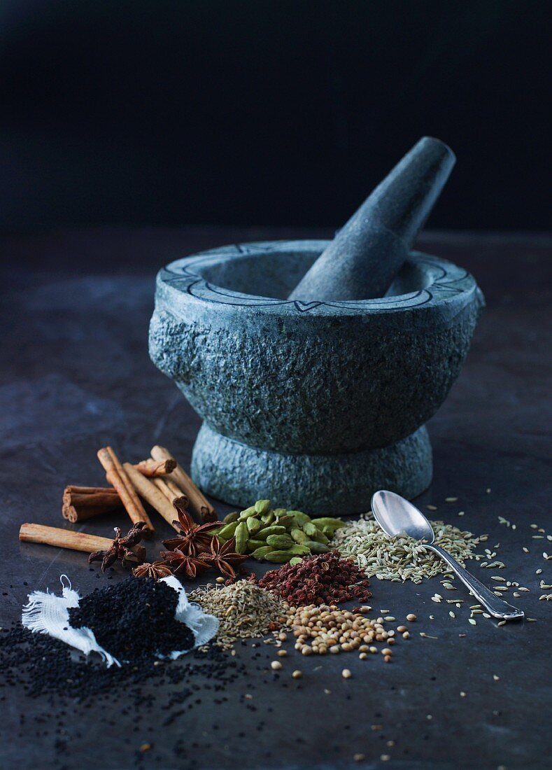 Various spices in front of a stone mortar