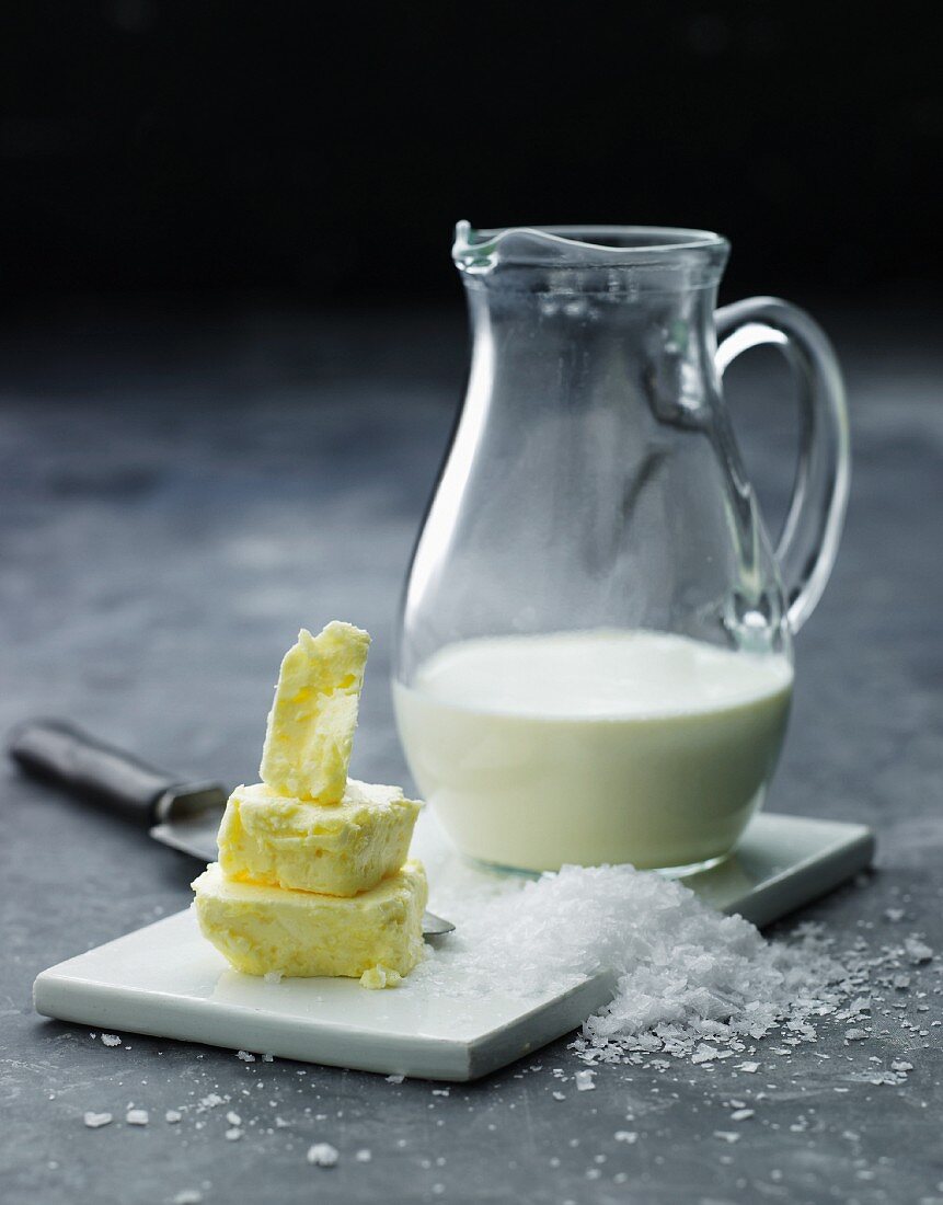 Stillleben mit Butterstückchen, grobem Salz & Milch im Glaskrug