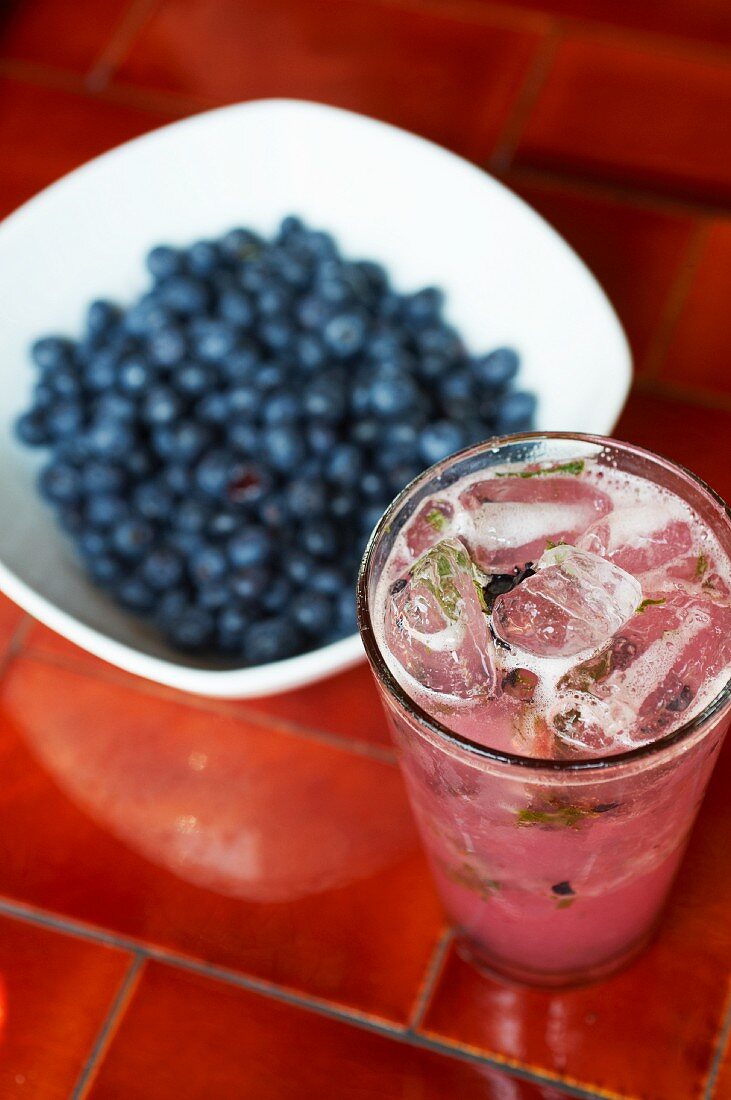 Blueberry Cocktail Made with Gin, Blueberries, Mint and a Simple Syrup; Bowl of Fresh Blueberries