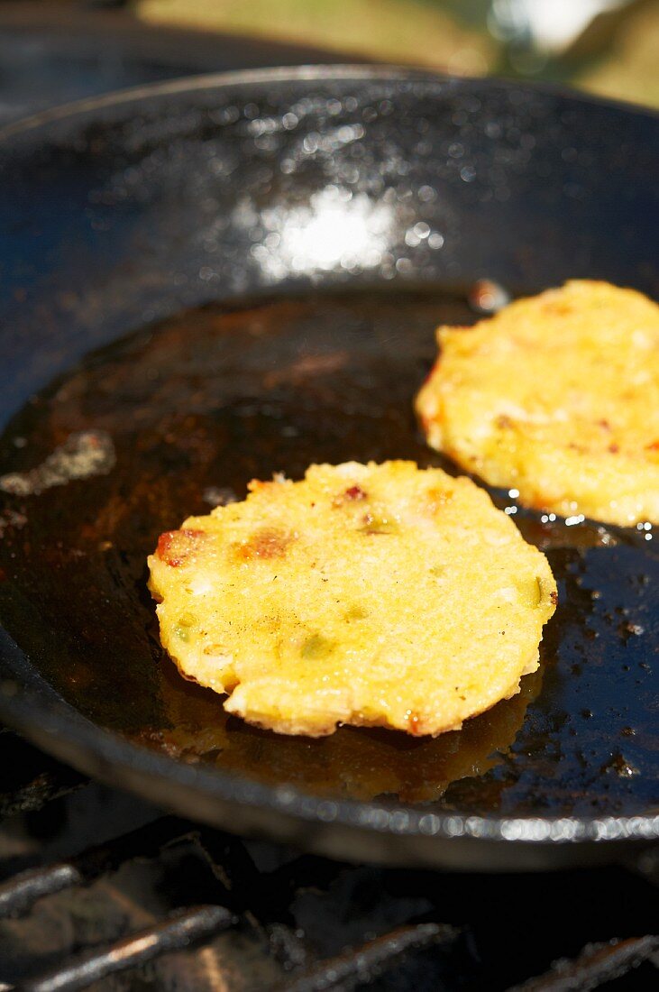 Two Corn Griddle Cakes Cooking in Cast Iron Skillet