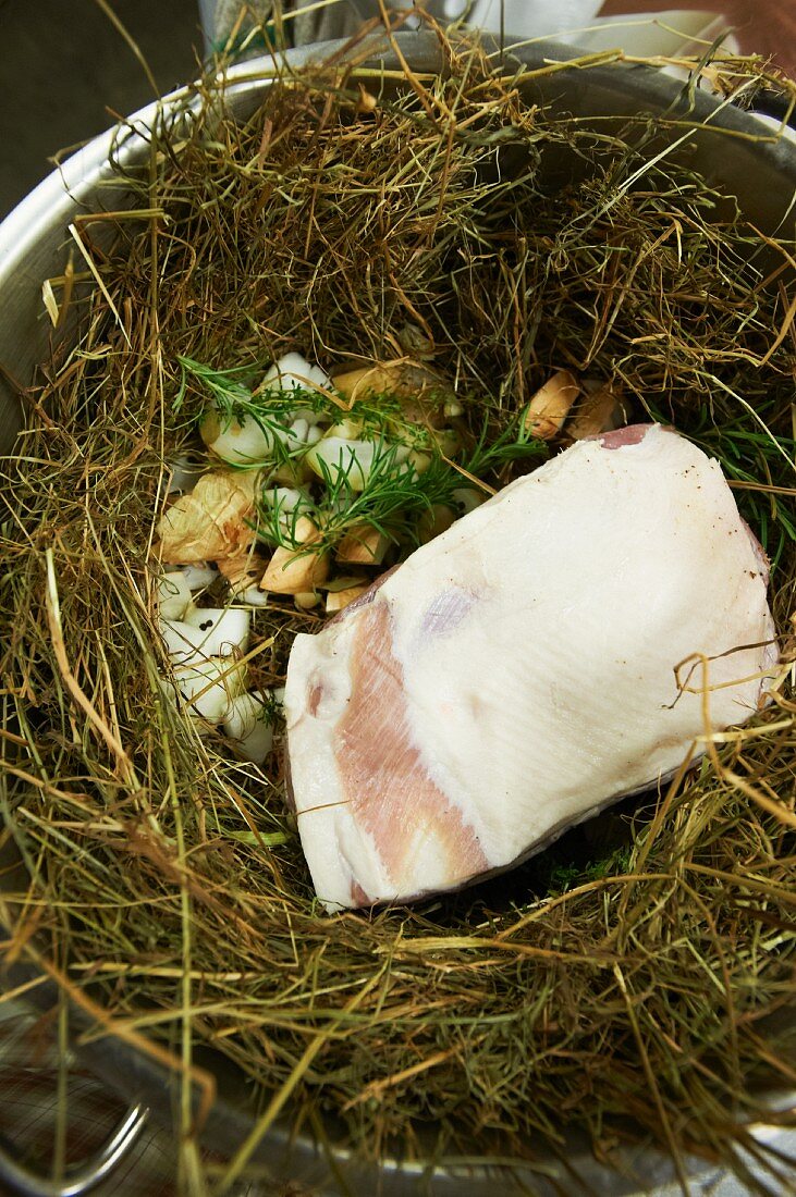 Rohe Schweineschulter mit Kräutern und Knoblauch auf einem Heubett