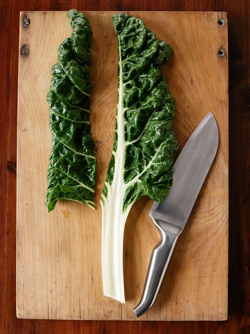 A chard leaf and a knife on a chopping board