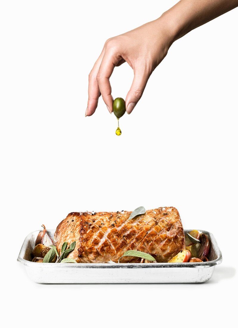 Hand presst Olivenöl aus Olive auf Schweinebraten mit Apfel und Salbei