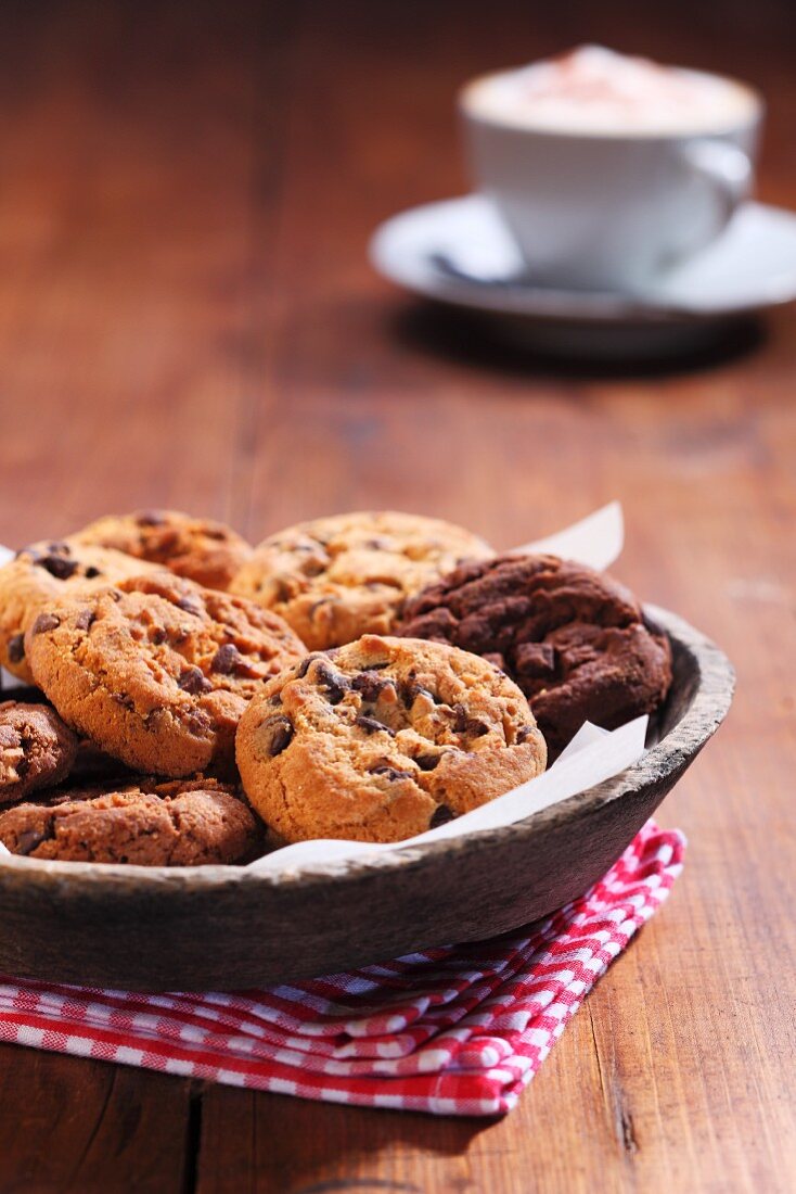 Chocolate chip cookies in a wooden bowl with a cappuccino in the background