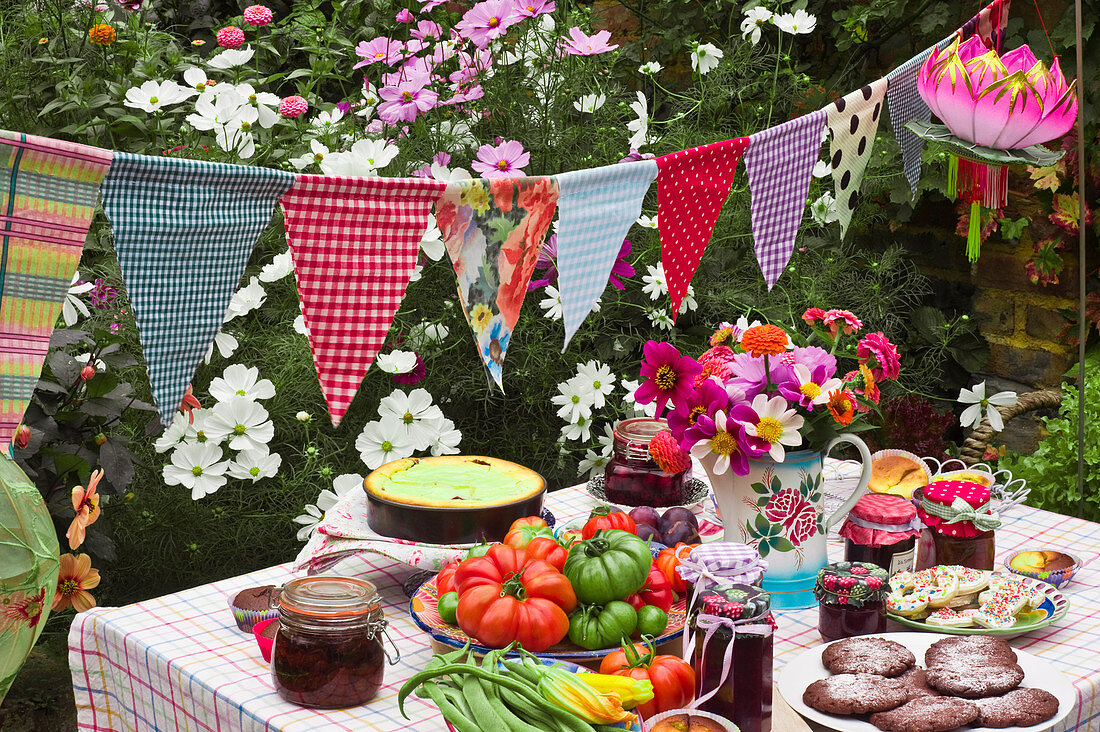 Gedeckter Tisch mit Plätzchen, frischem Gemüse, Marmeladen und Kuchen im Garten