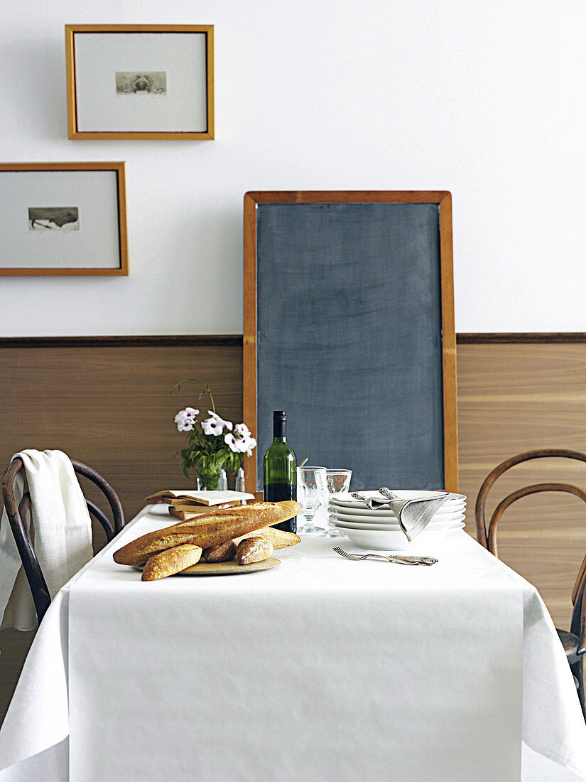 Weiß gededckter Tisch mit Baguette, Tellerstapel und Schiefertafel