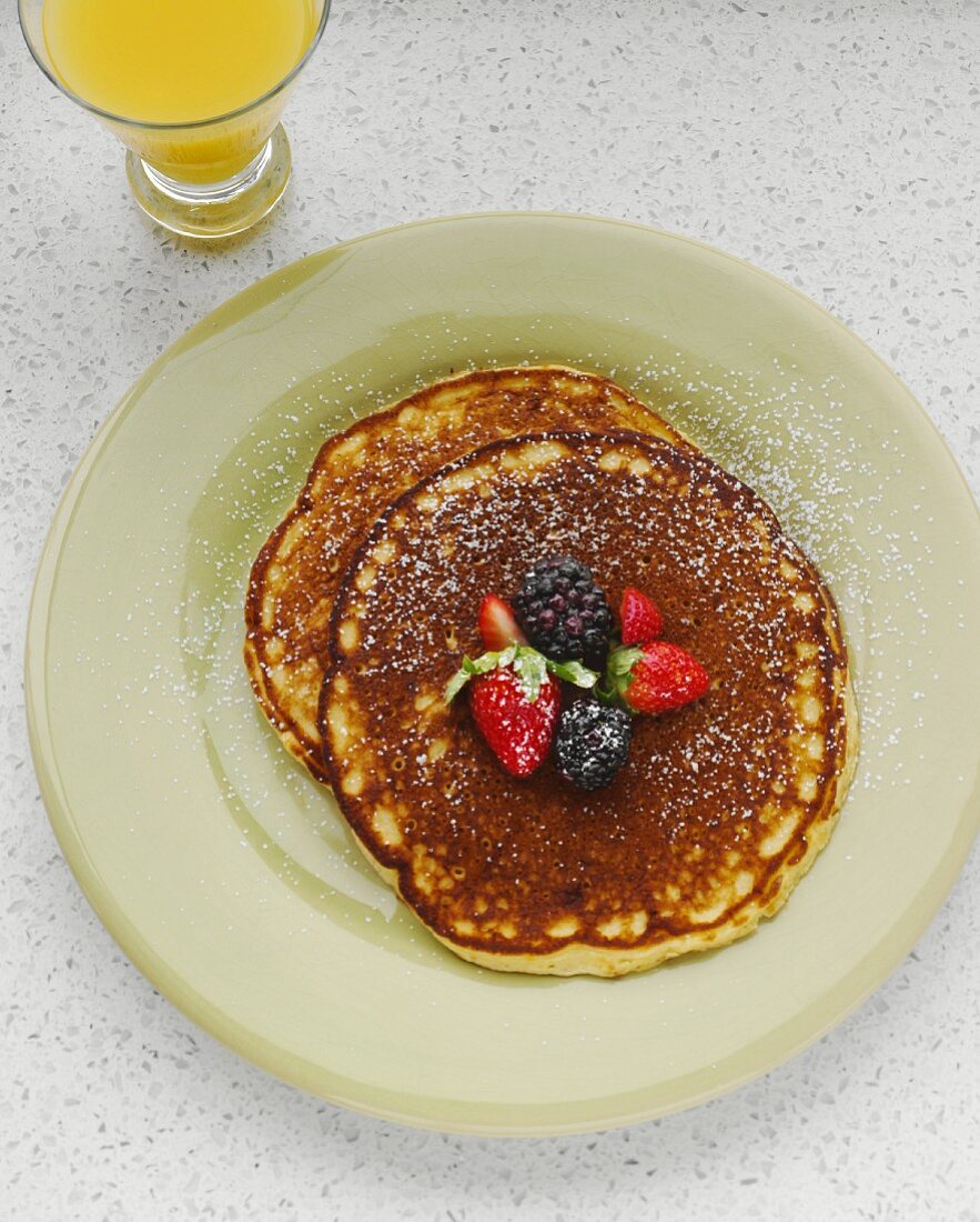 Organic Lemon Pancakes Topped with Berries and Powdered Sugar; Glass of Orange Juice