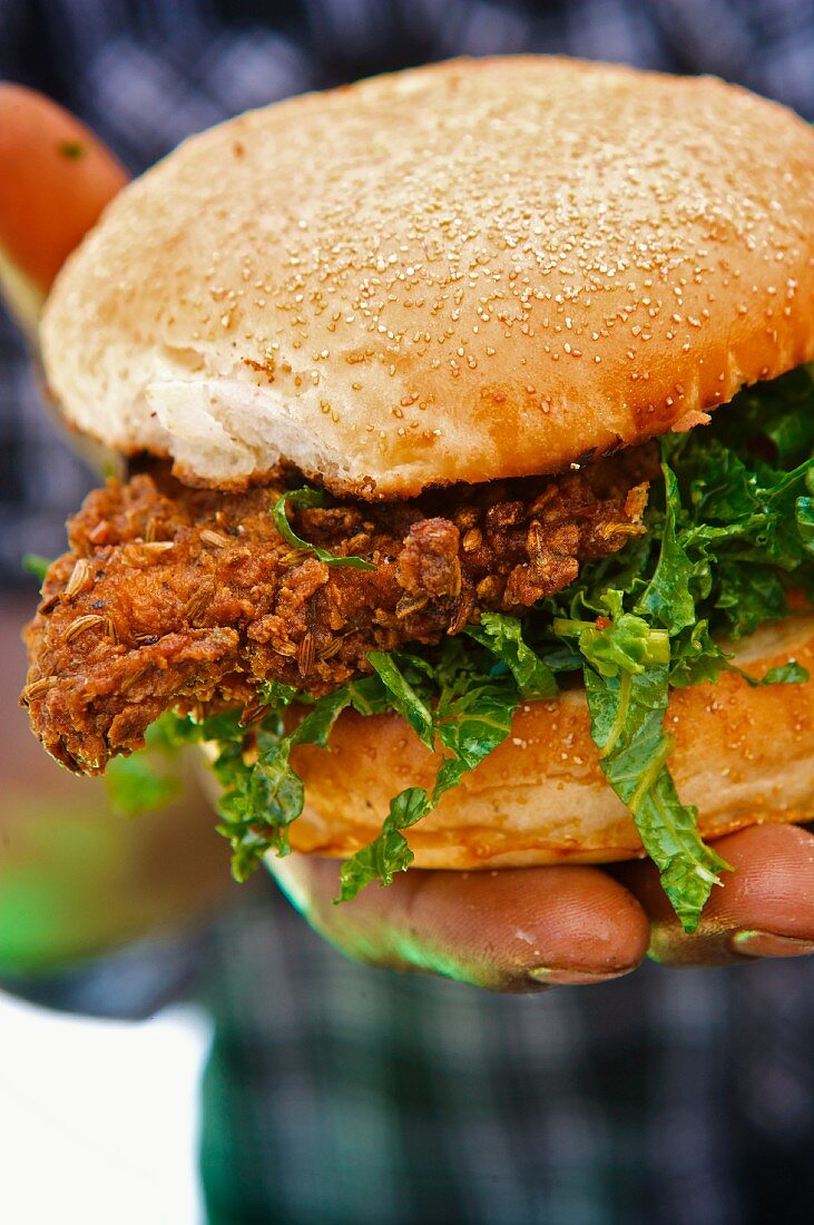 Person Holding a Fried Chicken Sandwich with Lettuce on a Bun