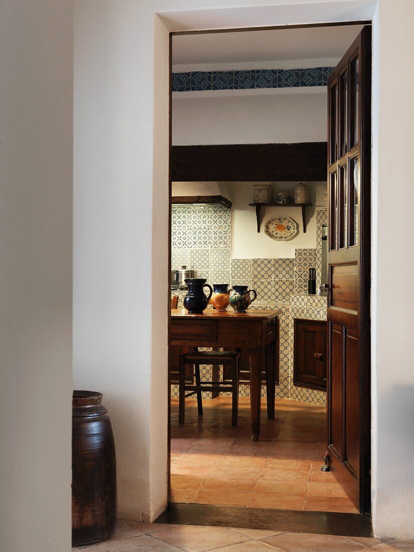 View from foyer through open door into Mediterranean kitchen with kitchen table and antique wall tiles