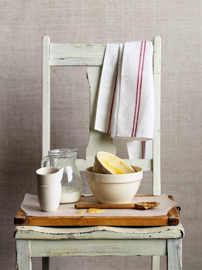Dirty mixing bowls, a jug of milk and a wooden spoon on a wooden chair