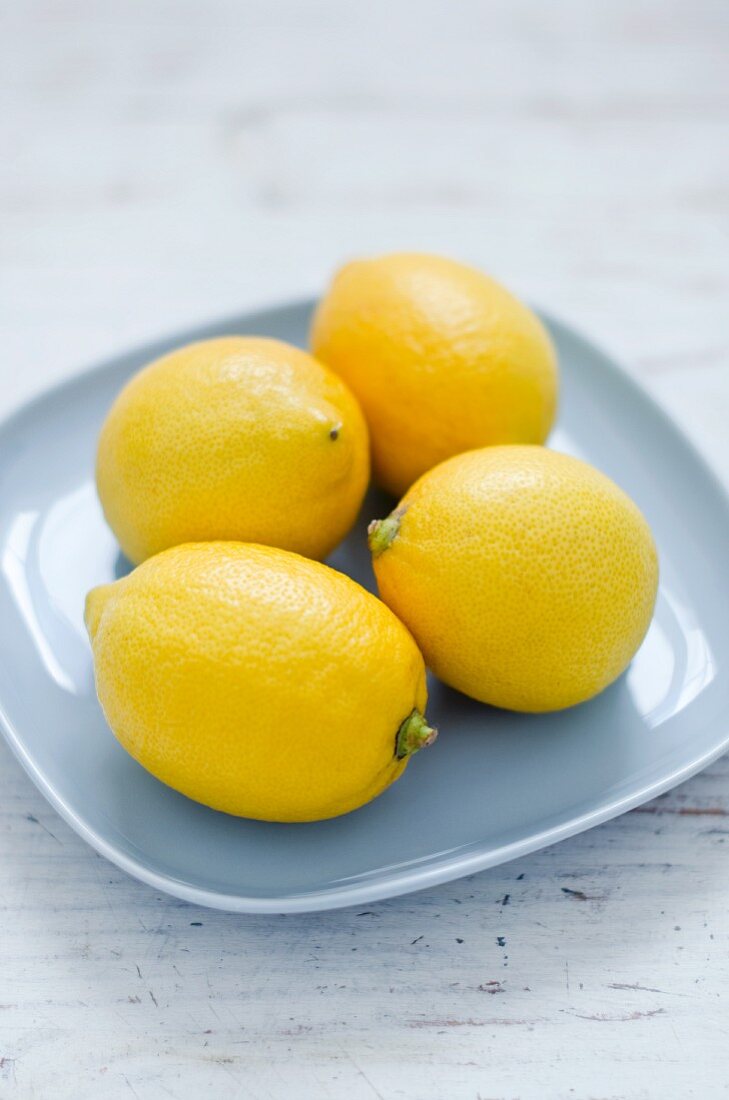 Vier Zitronen auf hellblauem Teller