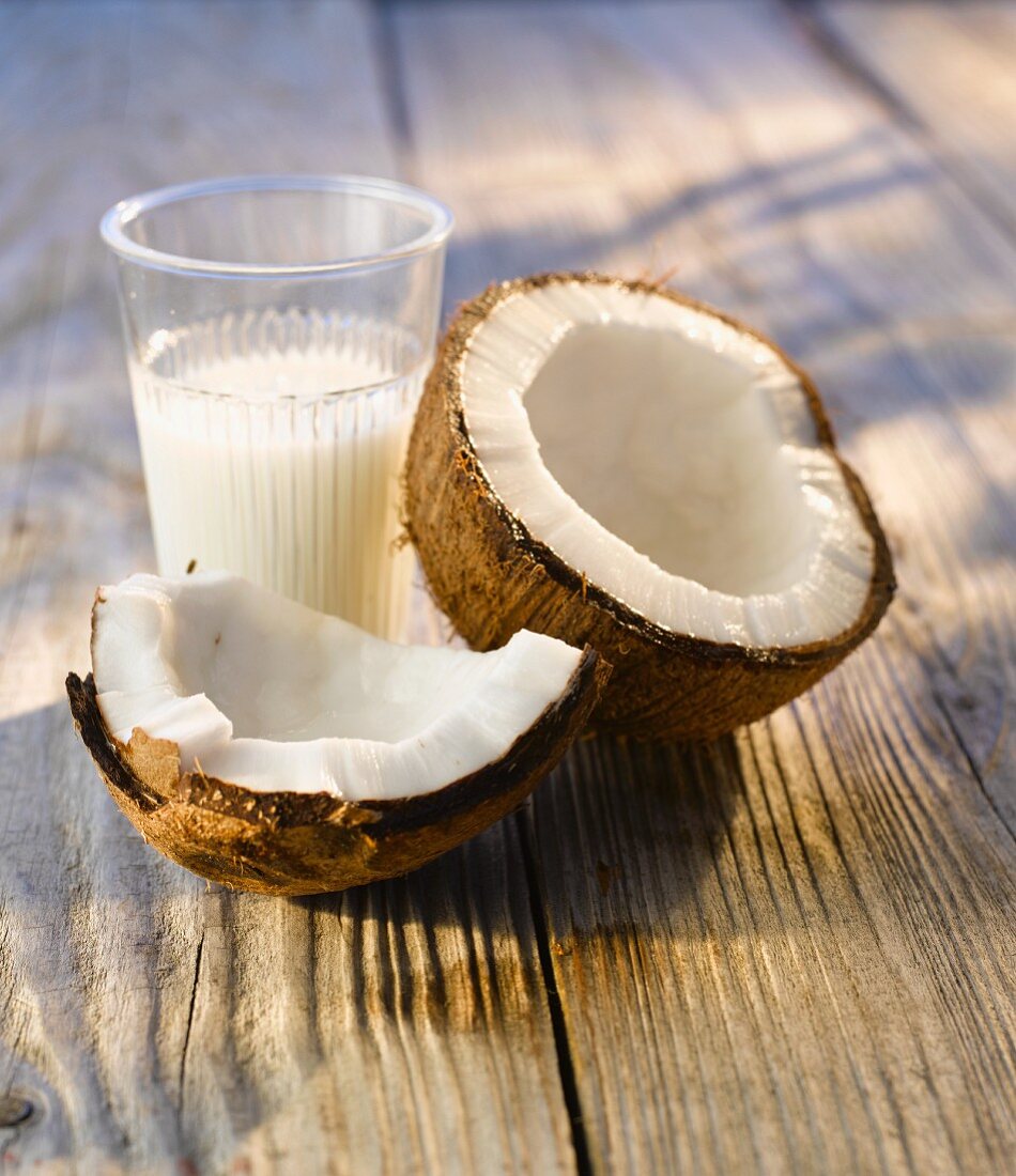 Aufgeschlagene Kokosnuss und ein Glas Kokosmilch