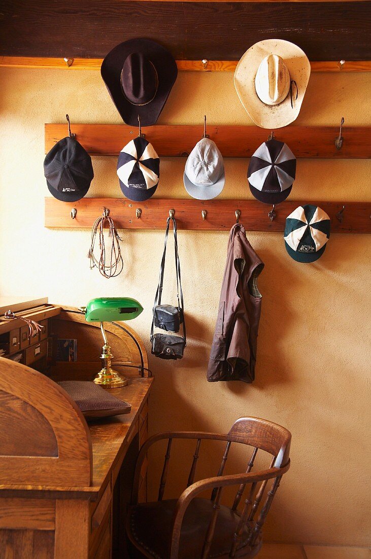 Hats and caps hanging on pegs above wooden, vintage-style desk and chair