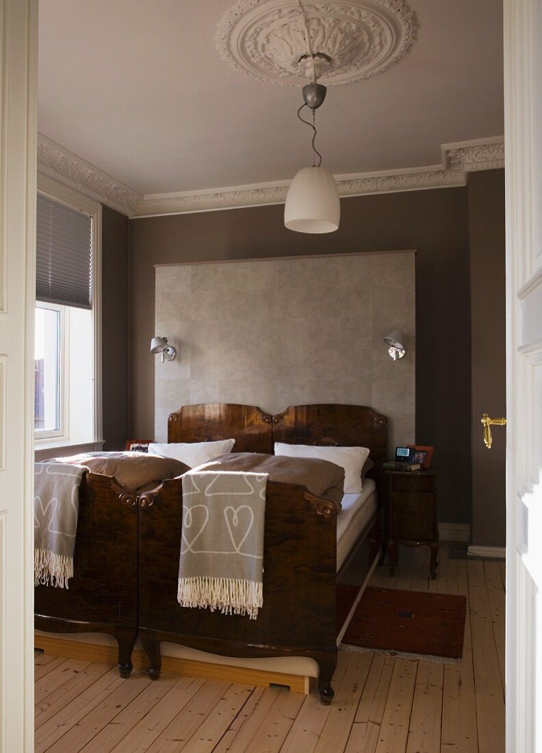 Antique twin beds standing next to one another against grey-painted walls with stucco frieze