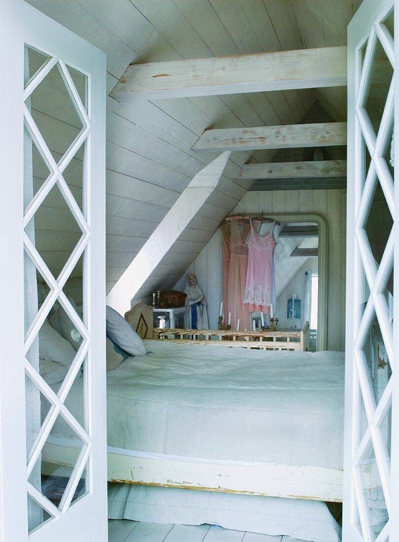 View through open doors of bed in converted attic with wood-panelled walls