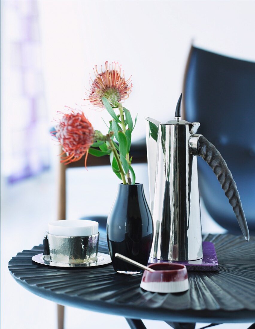 Kaffeepause - Kanne aus Chrom und Blumenvase mit roter Blume auf Beistelltisch