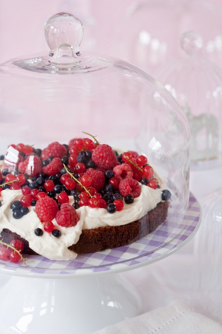 A chocolate cake topped with berries and cream on a cake stand