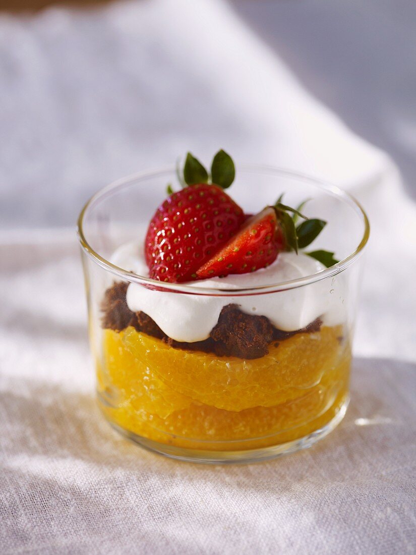 A layered desert with oranges, chocolate cake, cream and strawberries