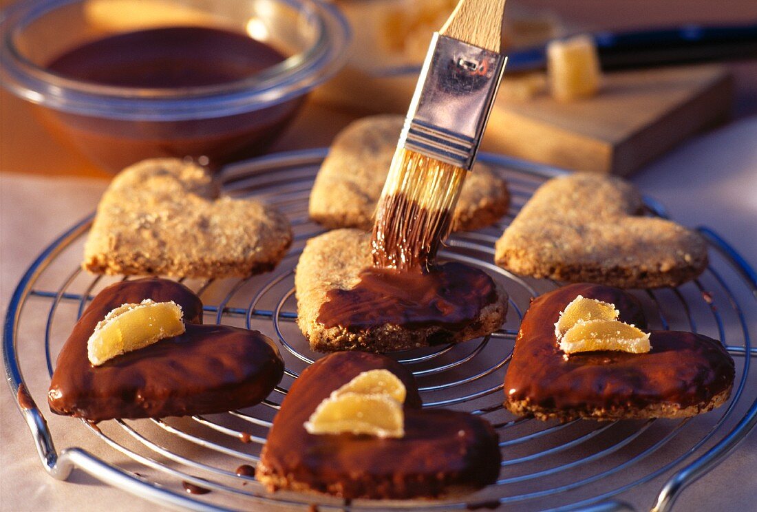 Heart-shaped ginger and chocolate biscuits being brushed with melted chocolate