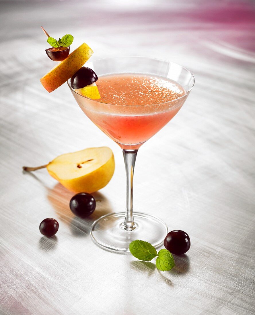 A fruit martini in a glass with fruit kebabs