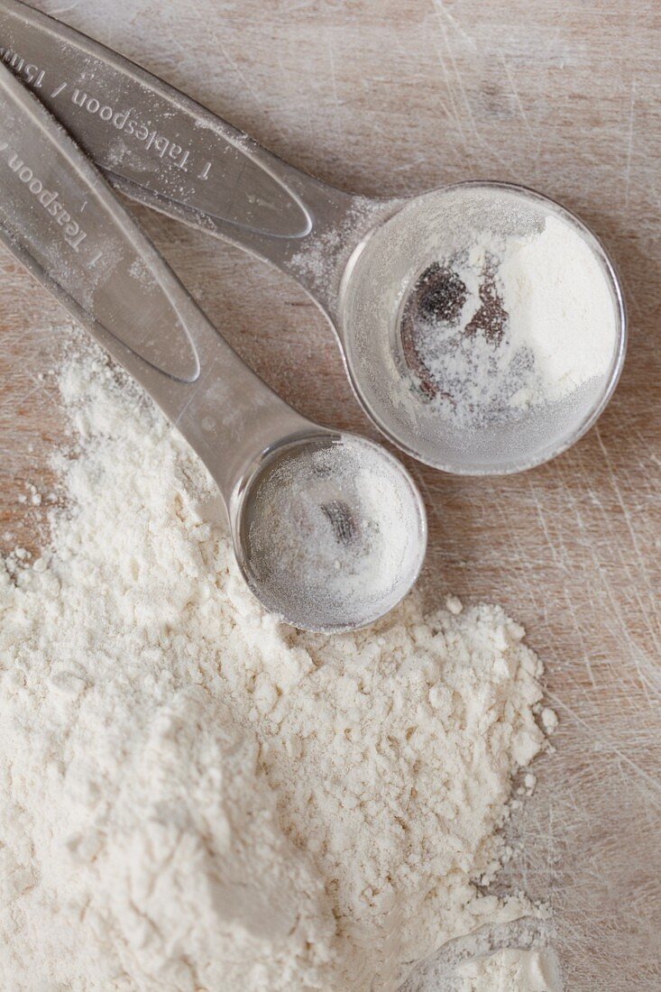 Two measuring spoons next to a pile of flour (seen from above)