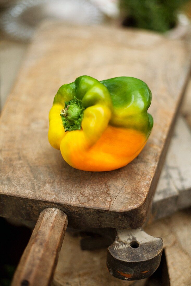 A yellow and green pepper on a wooden board
