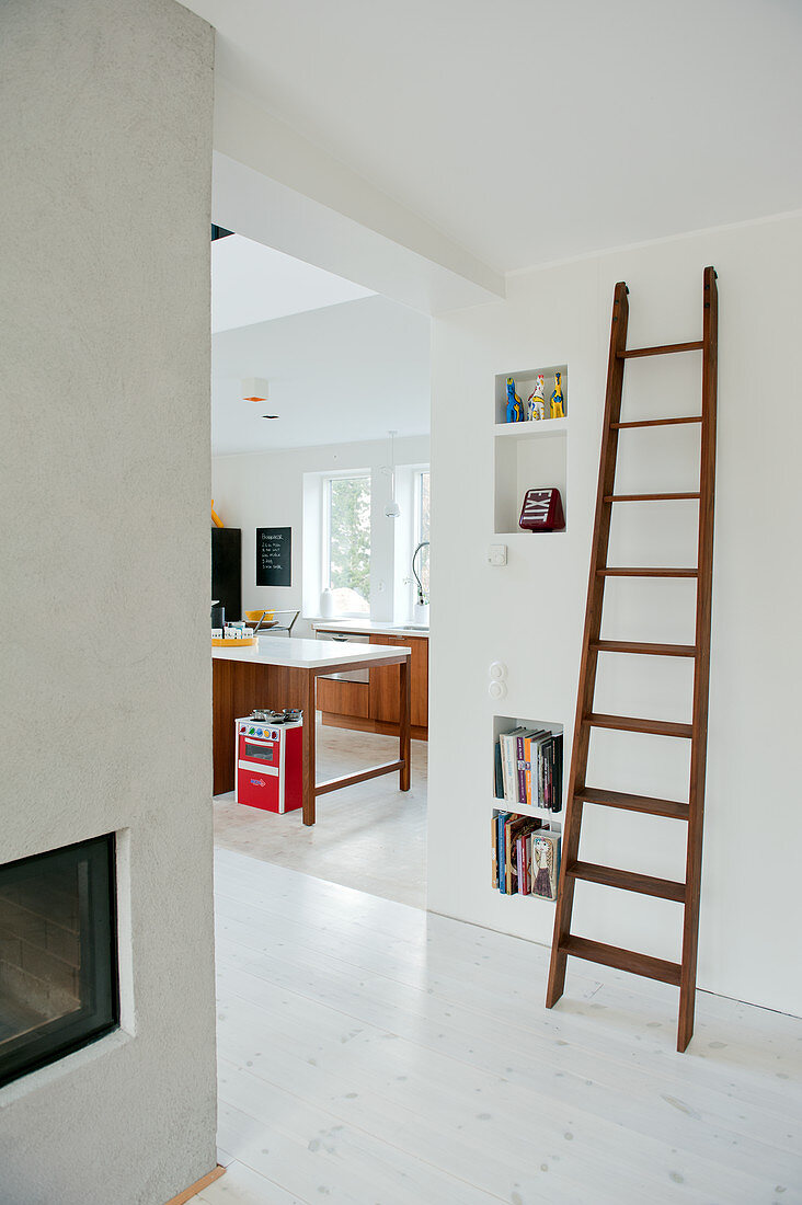 Old wooden ladder leaning on wall next to wide doorway showing view of modern kitchen beyond