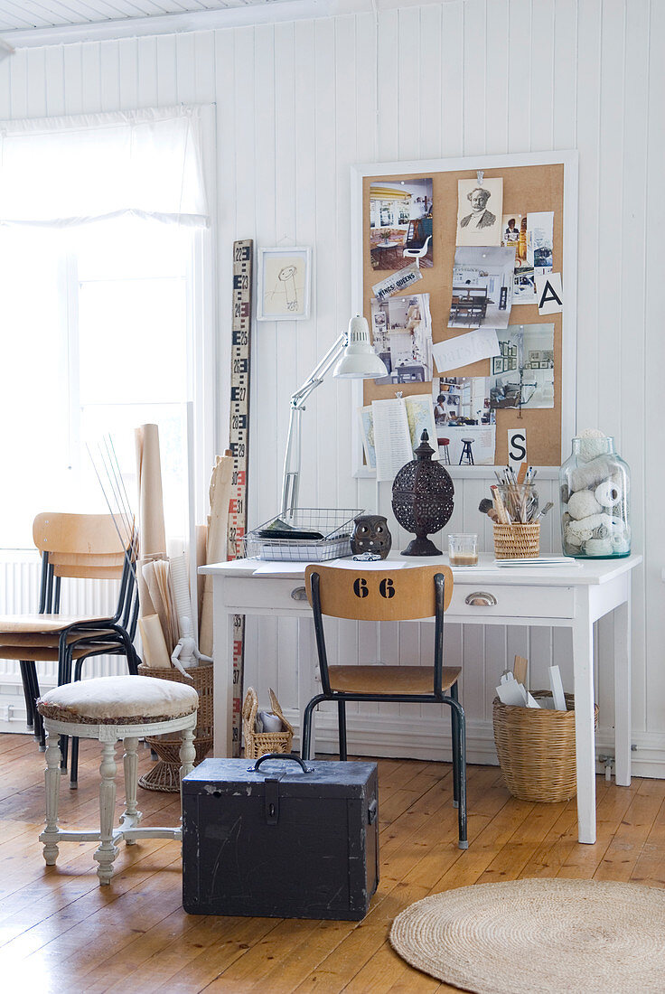 Vintage stool and trunk in front of desk against white-painted wooden wall with pinboard
