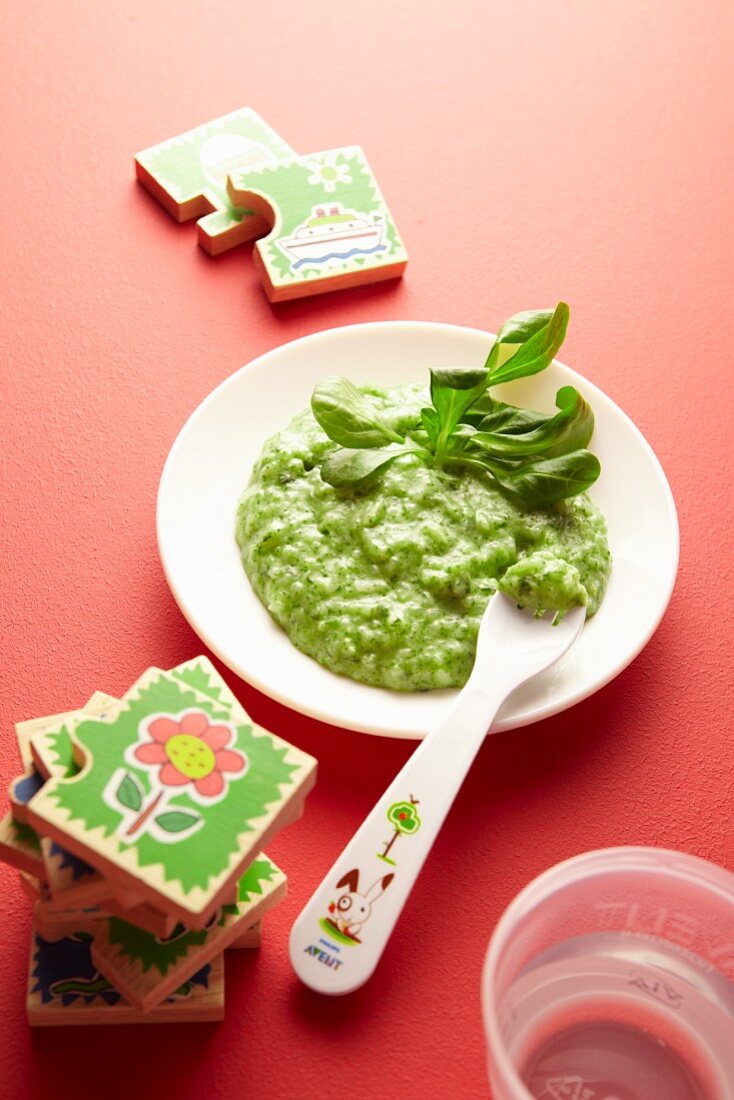 Baby food with green vegetables on a plate next to toys