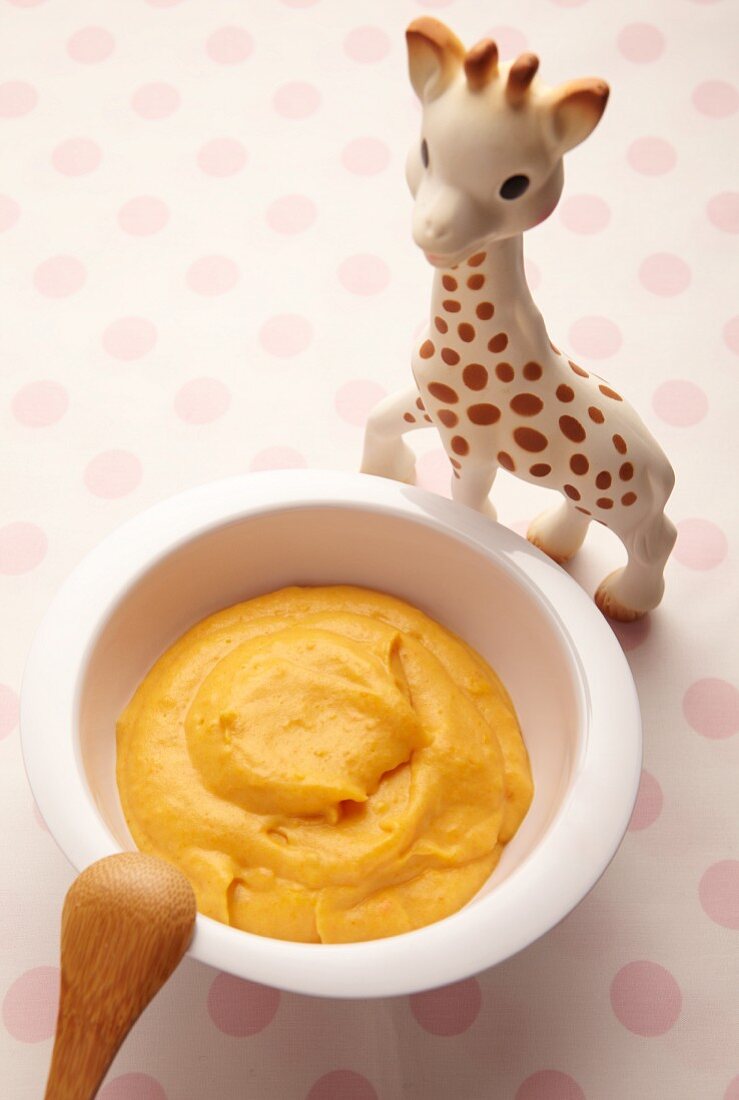 Carrot puree in a little dish next to a toy giraffe