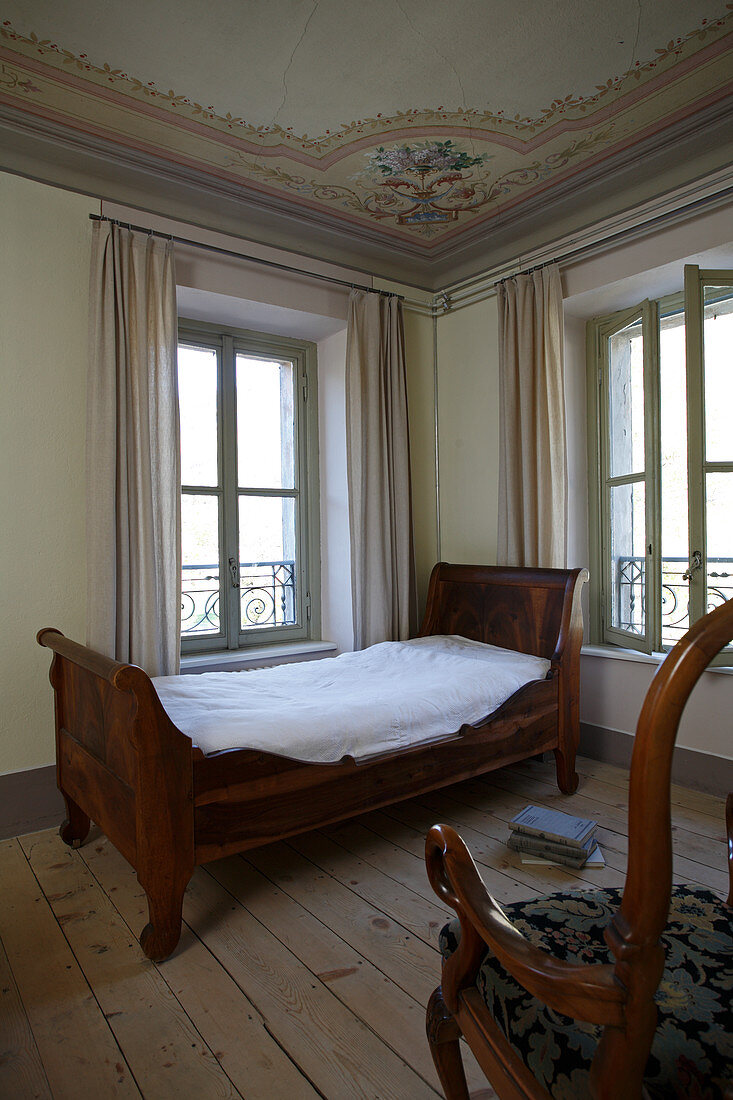 Antikes Bett vor dem Fenster in Schlafzimmerecke mit Deckenbemalung
