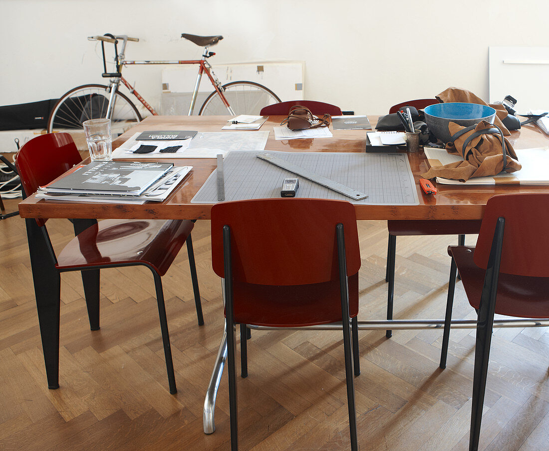 Arbeitsutensilien auf Tisch und Stühle im Bauhausstil vor Wand mit geparktem Fahrrad