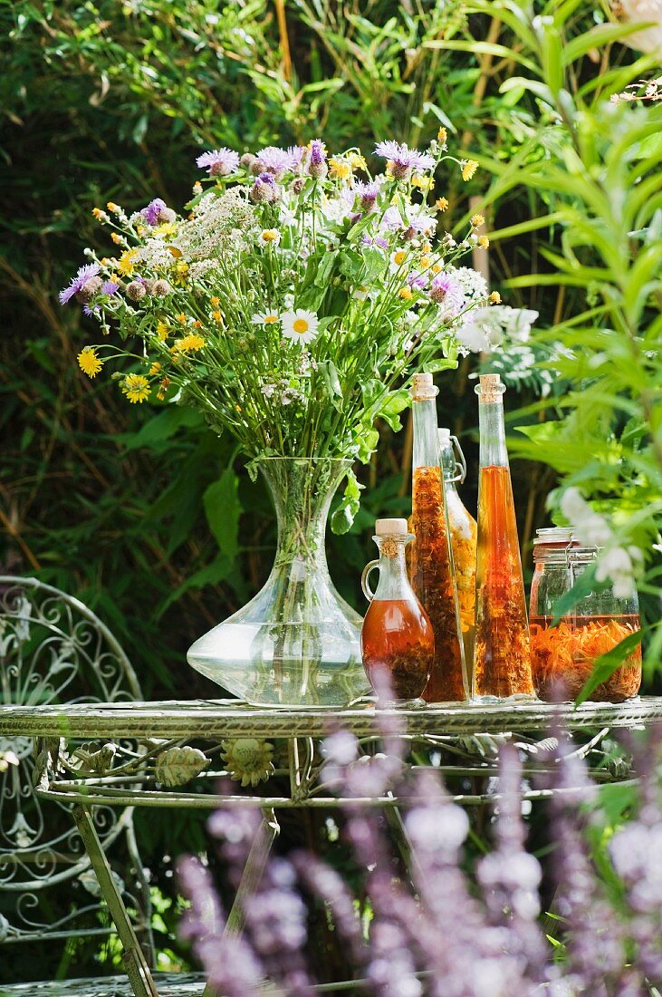 Wiesenblumenstrauss und Kräuteressenzen auf Gartentisch