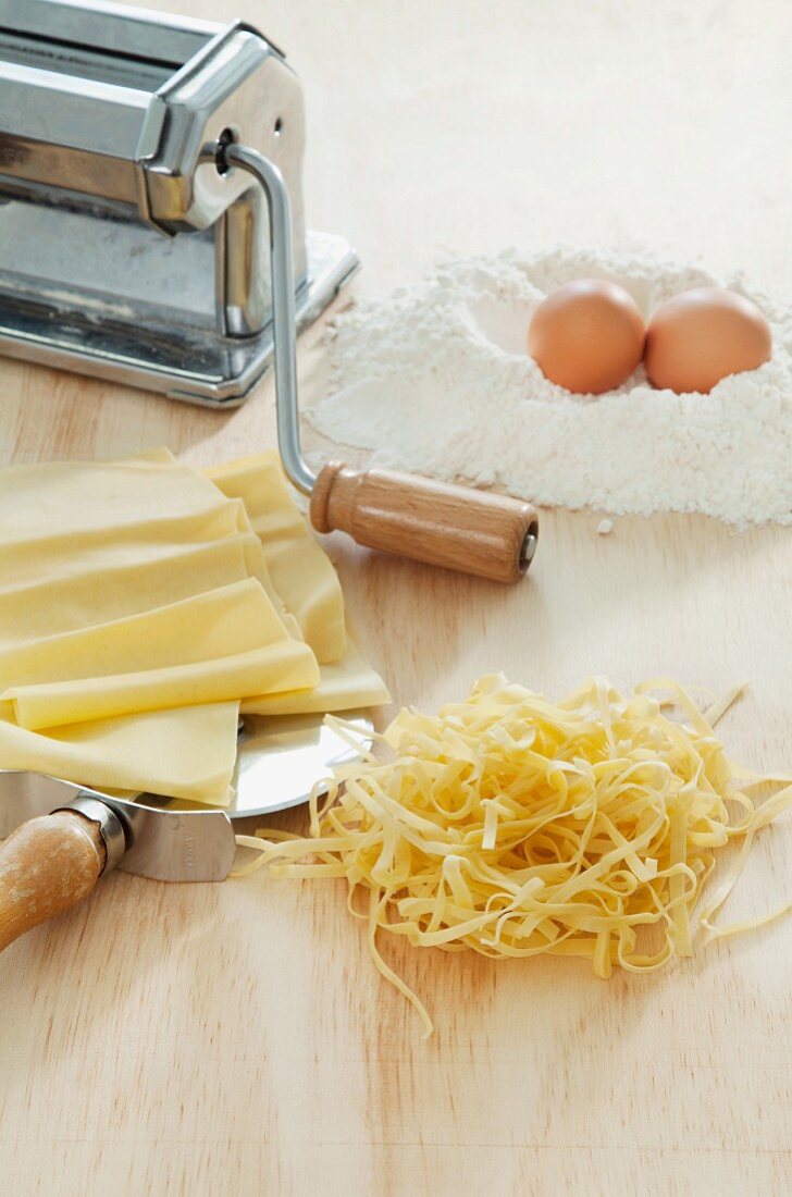 Homemade tagliatelle, a pasta maker, flour and eggs