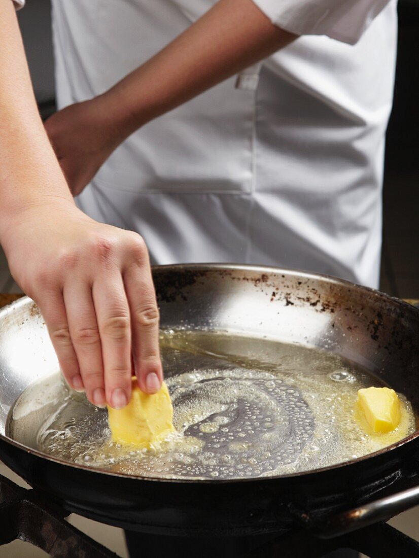 Koch schmelzt Butterstücke in der Pfanne