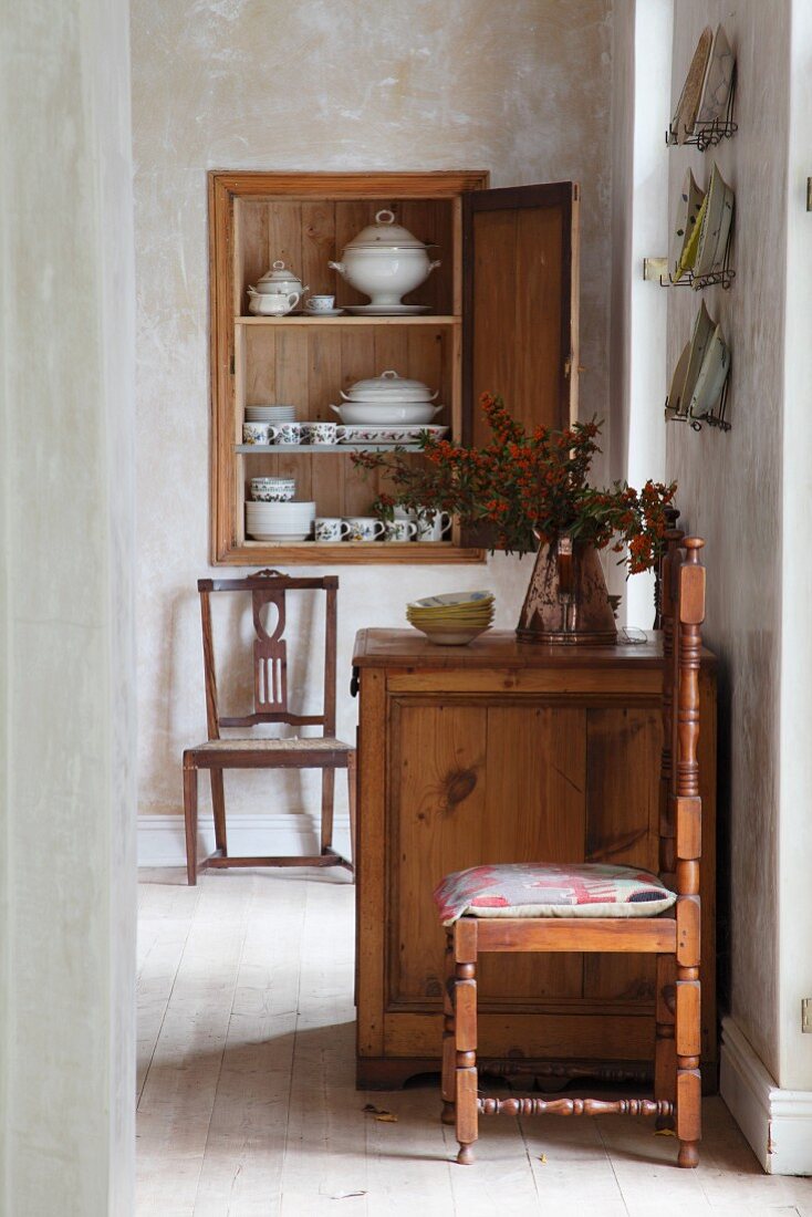 View through floor-to-ceiling doorway of rustic chest of drawers and kitchen chairs in simple dining room