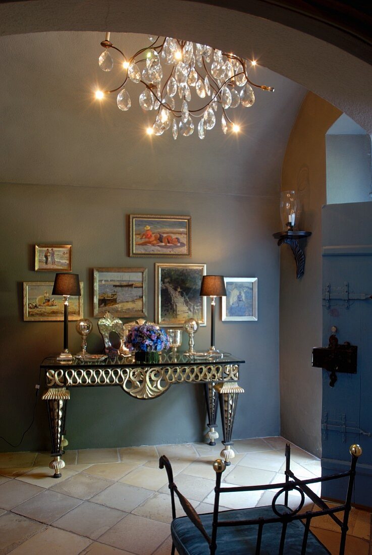 Elegante Konsole, eingerahmte Bilder und Kristallkronleuchter in einer Diele mit Terrakottafliesboden