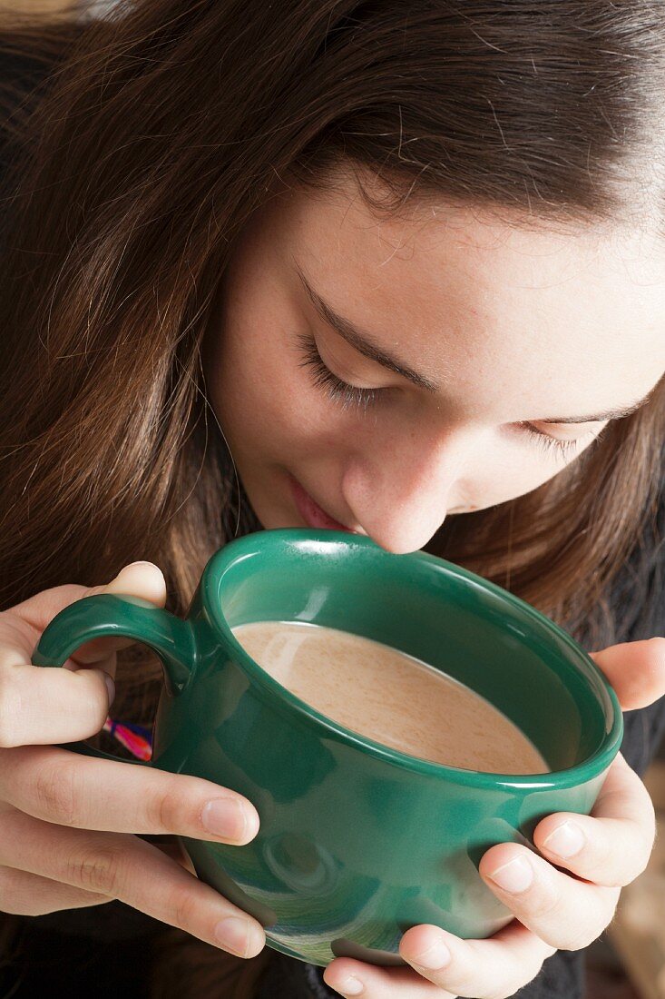 Junge Frau riecht an einer Tasse Caffe Latte