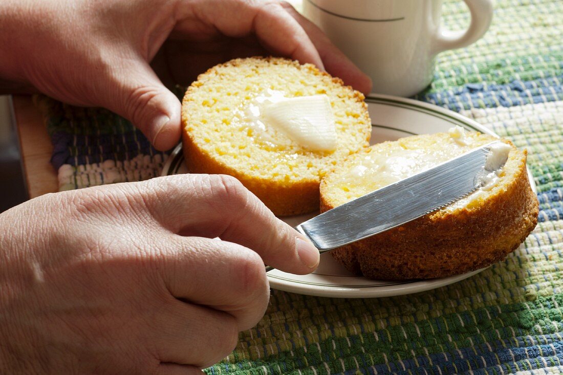 Mann streicht Butter auf Maismuffin