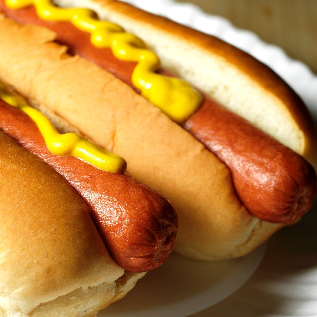 Two Hot Dogs on Buns with Mustard; On Paper Plate; Close Up