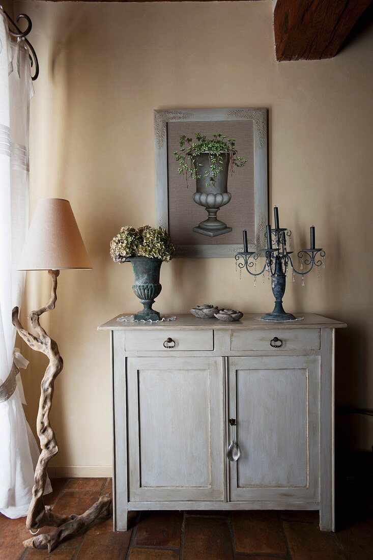 Stone vase and candelabra on wooden cabinet next to rustic standard lamp