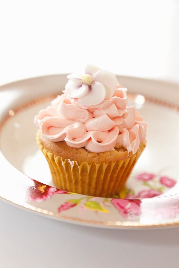 A cupcake topped with frosting and sugar flowers on a plate