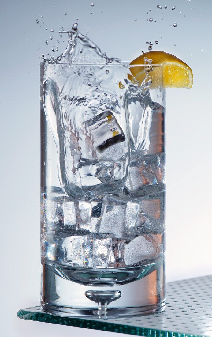 Ice Cubes Splashing into a Glass of Water with a Lemon Wedge