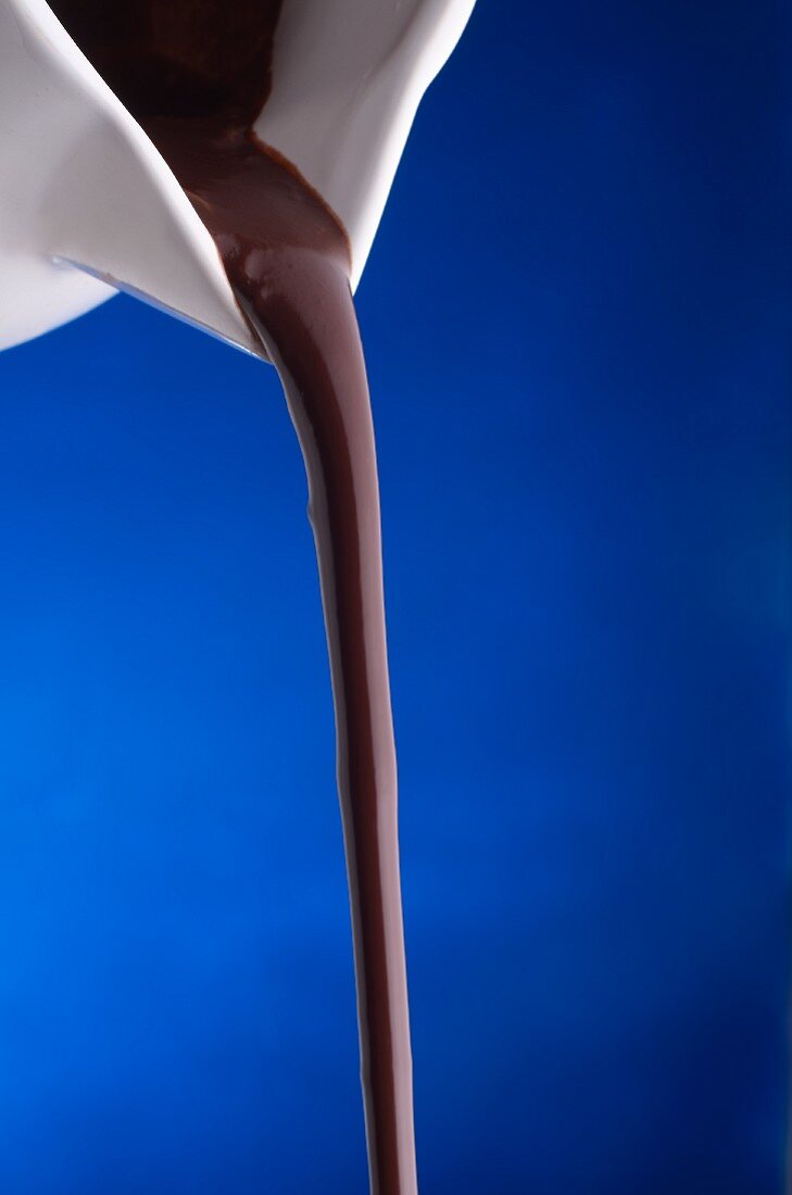 Chocolate Sauce Pouring From a White Pitcher Against a Blue Background
