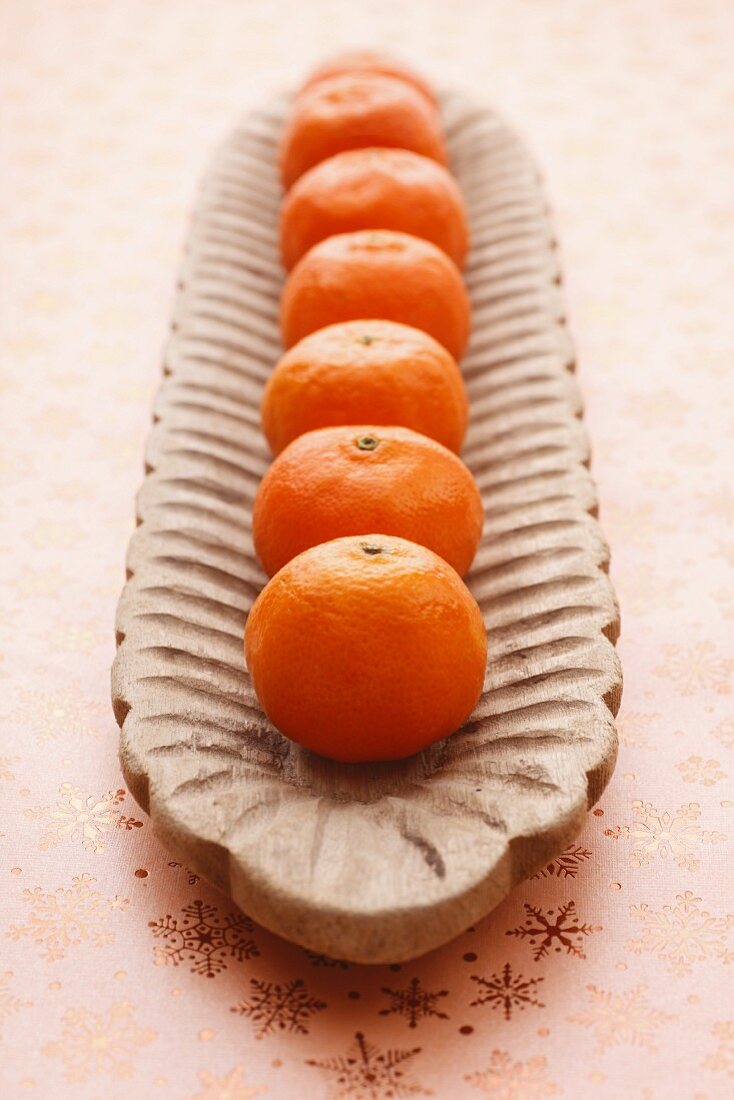 A row of mandarins in a wooden bowl