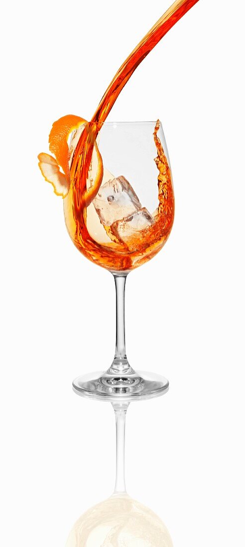 Aperol being poured into a glass with an ice cube