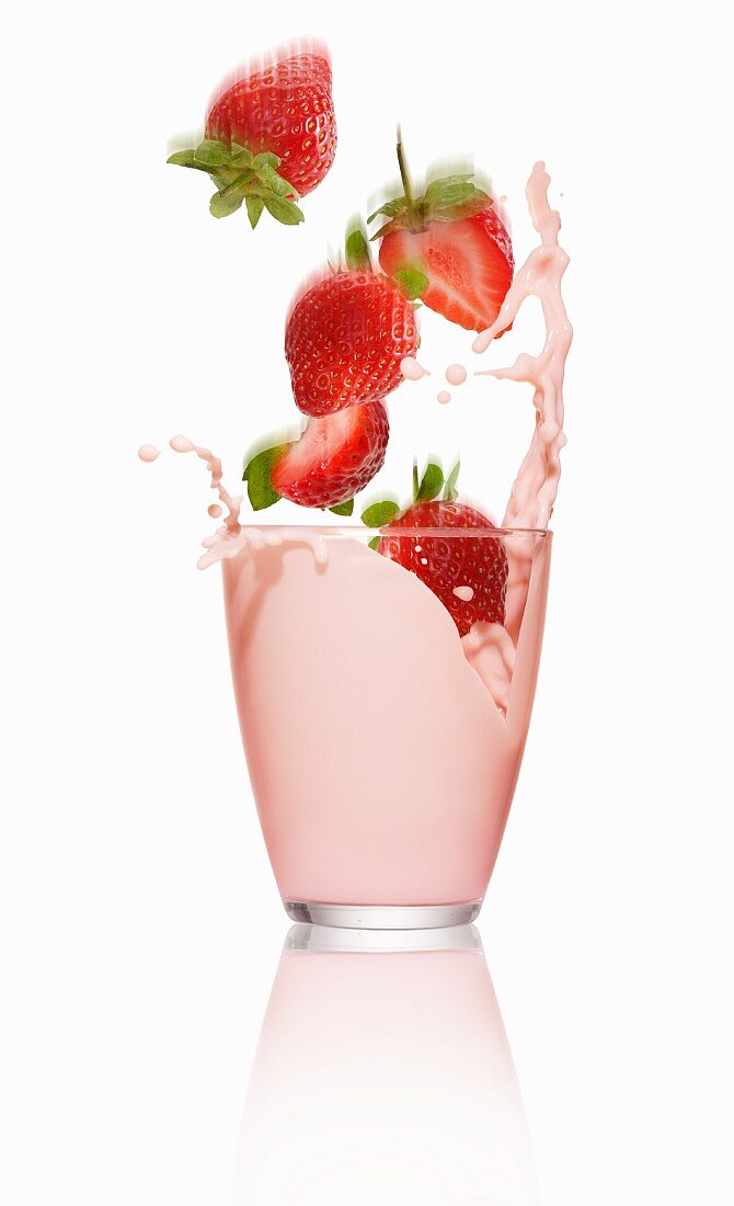 Erdbeeren fallen in ein Glas Erdbeermilch