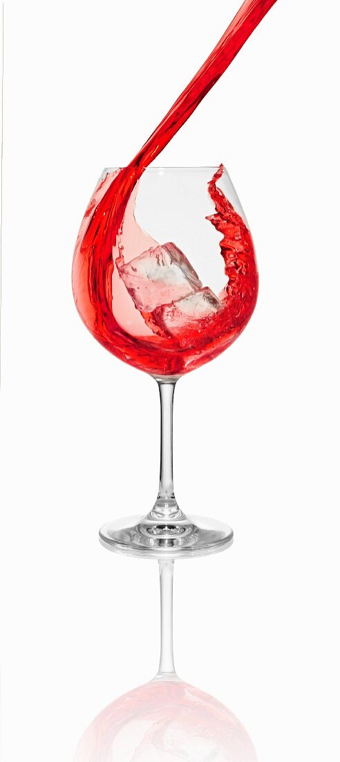 Roten Cocktail in ein Glas mit Eiswürfeln einschenken