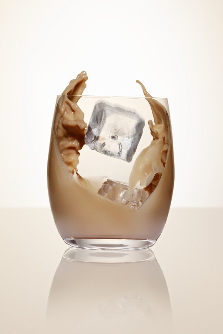 An ice cube falling into a glass of cream liqueur